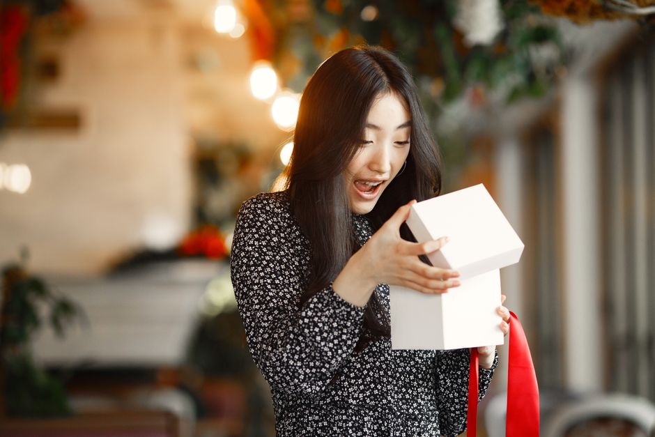 アジアの女性が室内で赤いリボンのついたギフトボックスを楽しそうに開けます。
