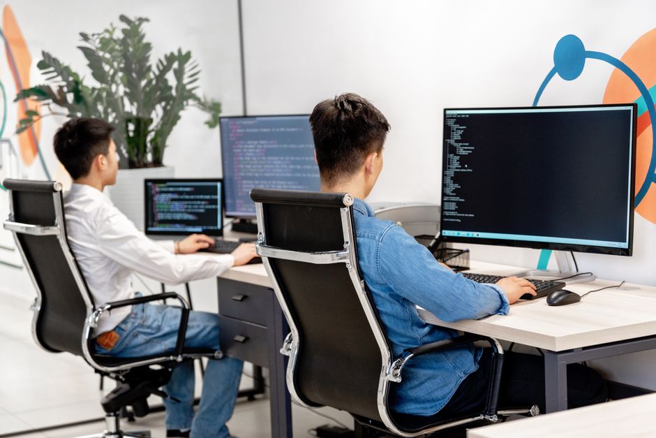 大きなモニターのある現代的なオフィスワークスペースでプログラミングをしている二人の男性開発者。
