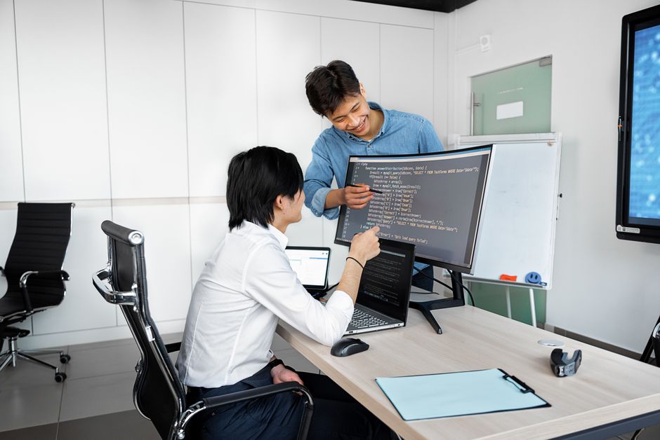 現代的なオフィス環境で、ノートパソコンとモニターを使ってデスクで協力する2人の若手プロフェッショナル。