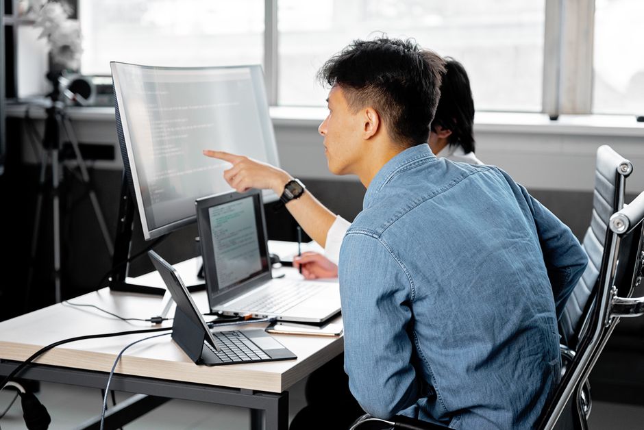 テクノロジー中心のワークスペースで、プロフェッショナルがノートパソコンとモニターを使って協力しています。
